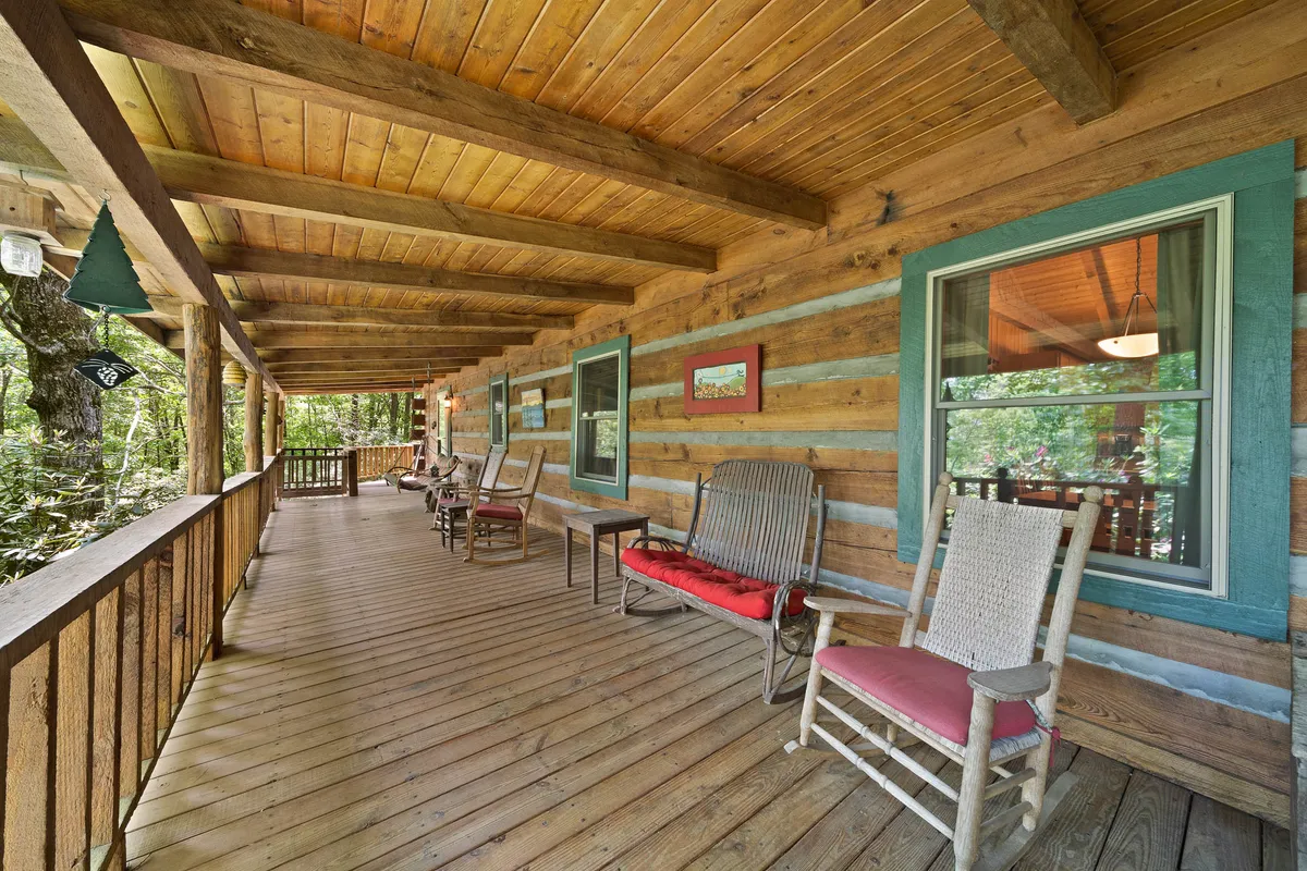 This image features wooden rocking chairs set on the porch of a log cabin, surrounded by lush greenery. The large windows hint at a cozy interior, and the natural setting provides a glimpse of the tranquil environment outside. The porch feels inviting and offers space for couples to relax together and enjoy the natural beauty.