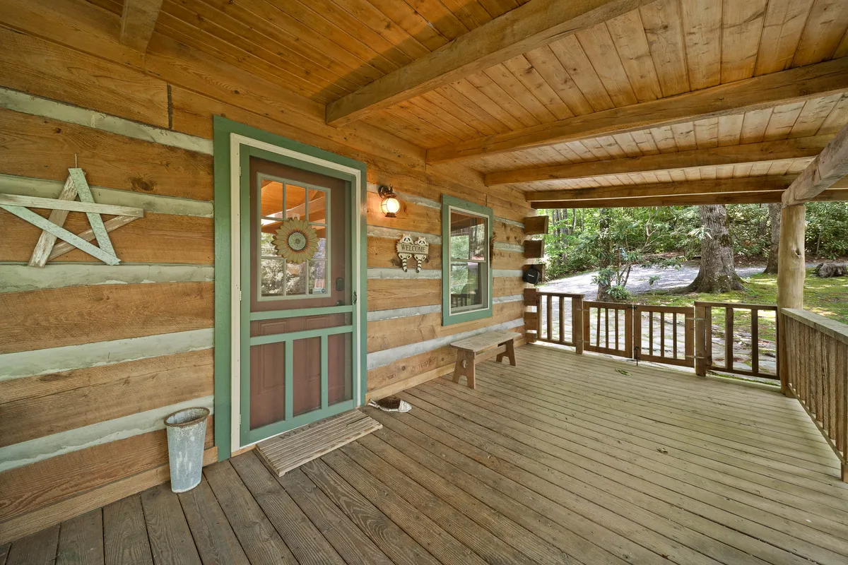 This image shows the front door of the cabin, framed by sturdy wooden beams and rustic log wall textures. Decorative elements like a star add charm, while windows offer inviting glimpses of the interior. The scene hints at people enjoying the outdoors and relaxing on the porch, with plenty of space for gathering.