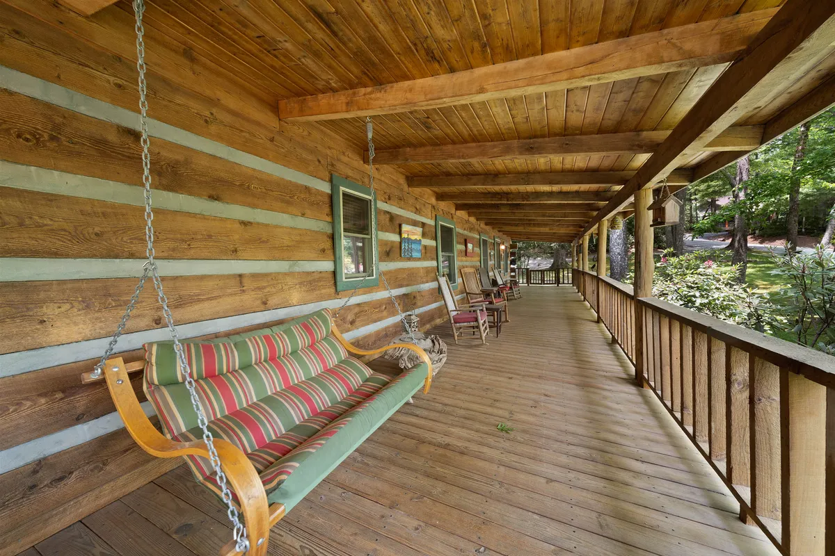 The image shows swinging benches on a wooden deck with sturdy railings and beams, overlooking trees beyond. The atmosphere is serene and the space provides a perfect spot to watch the sunset or share quiet moments outdoors with a partner.