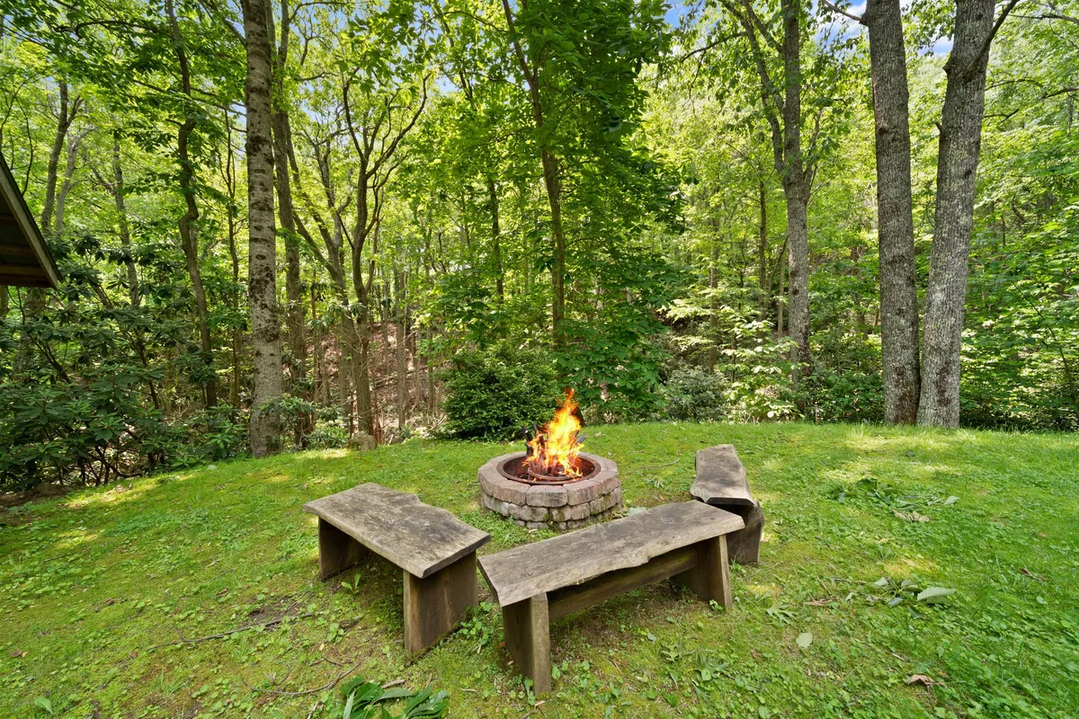 A rustic fire pit is surrounded by wooden benches and set amongst a backdrop of lush trees. The fire pit area is clearly designed for gatherings, storytelling, s'mores, and creating memories in the heart of nature—ideal for relaxing evenings after a day outdoors.
