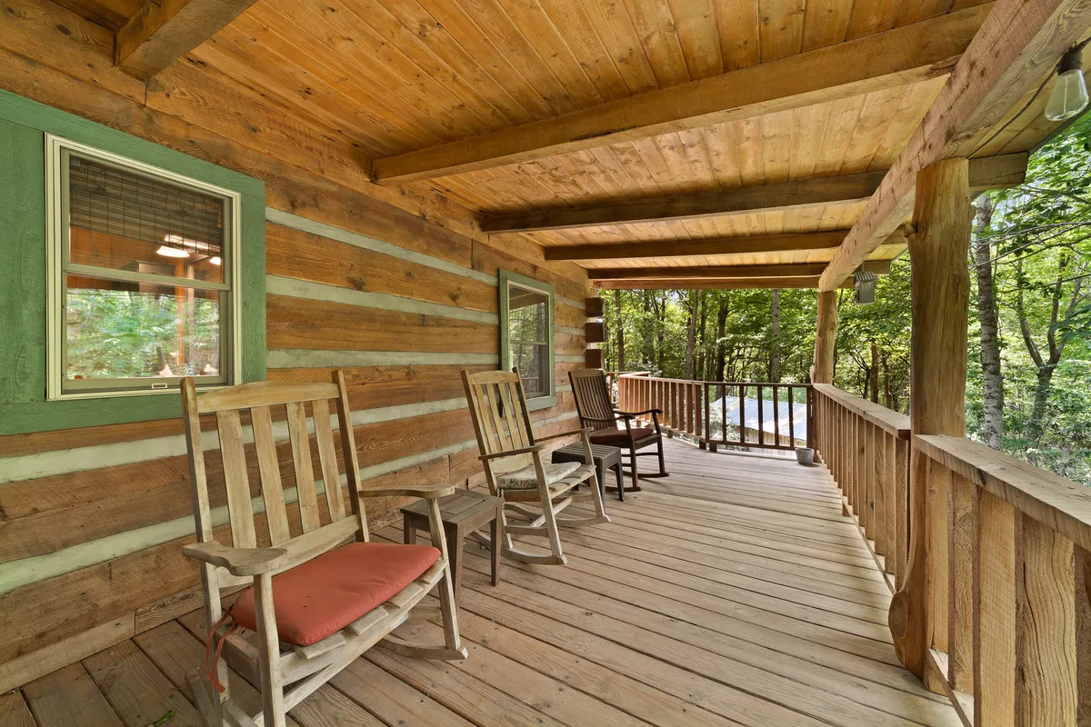 A tranquil exterior scene featuring classic rocking chairs on a wooden porch, set against the log cabin’s rustic walls. The area is surrounded by quiet natural beauty, inviting visitors to unwind, listen to nature, or watch a sunset.