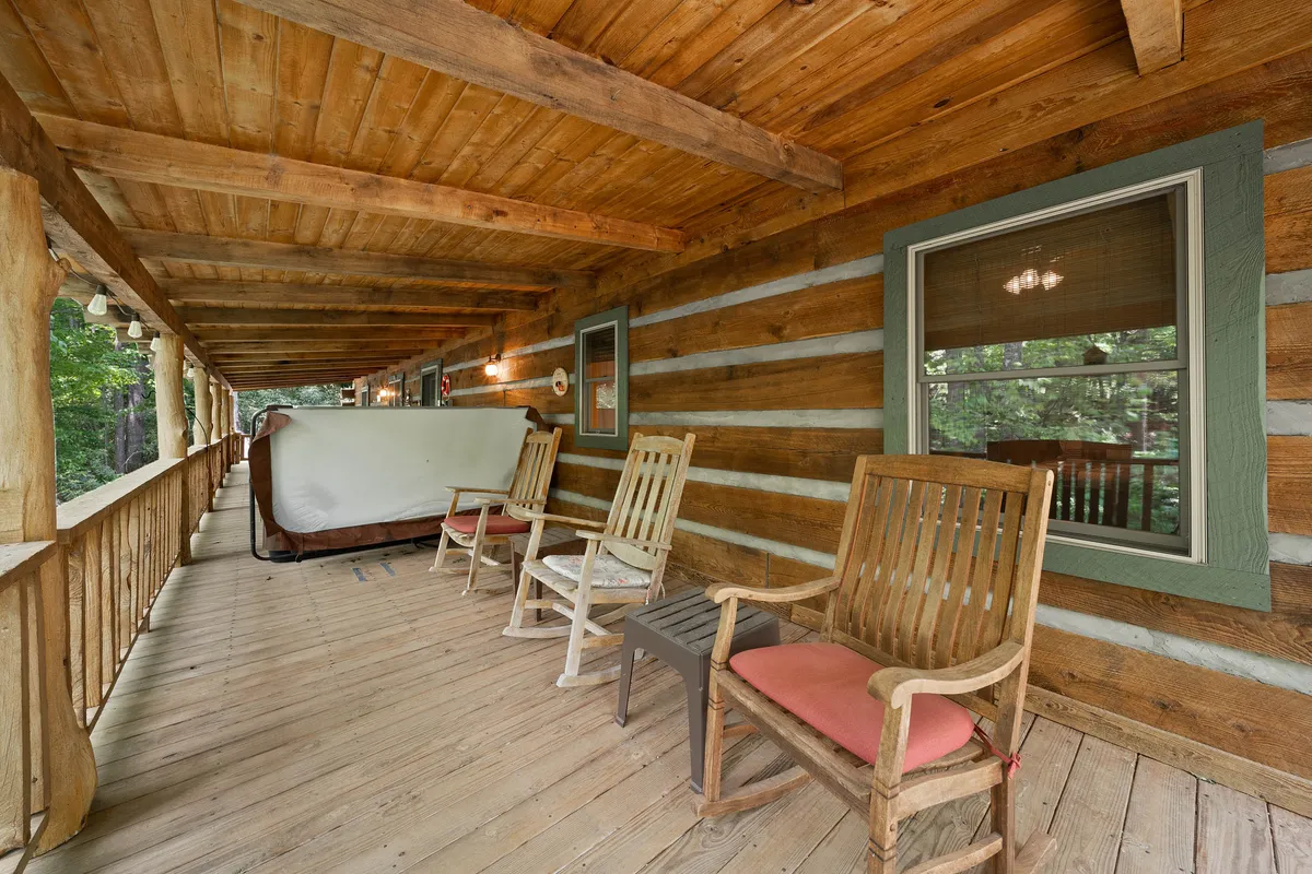 A cozy porch scene with wooden rocking chairs, the log cabin’s structure, and a backdrop of natural surroundings. The image highlights the inviting outdoor living space, ideal for soaking in sunrise views, sharing stories after a hike, or simply enjoying the sounds of the creek nearby.