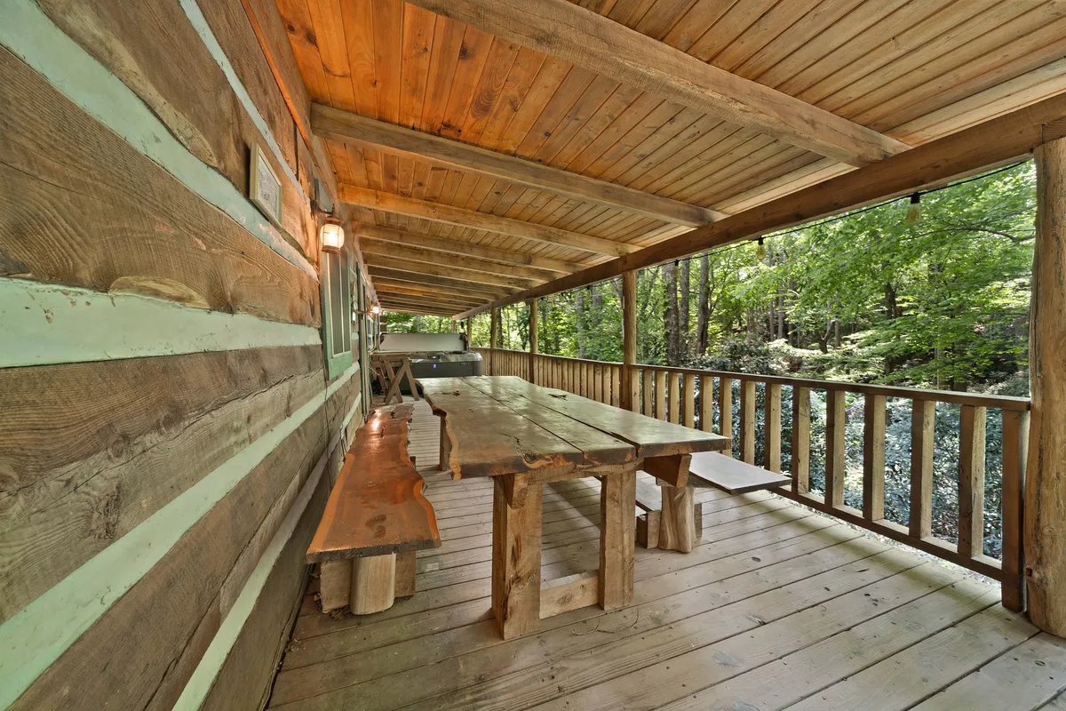 A long wooden dining table is set under a covered outdoor structure, surrounded by lush greenery. The space is perfect for alfresco meals with family or friends, offering sheltered comfort while remaining immersed in the mountain landscape. The communal setup emphasizes togetherness and the enjoyment of fresh air dining.