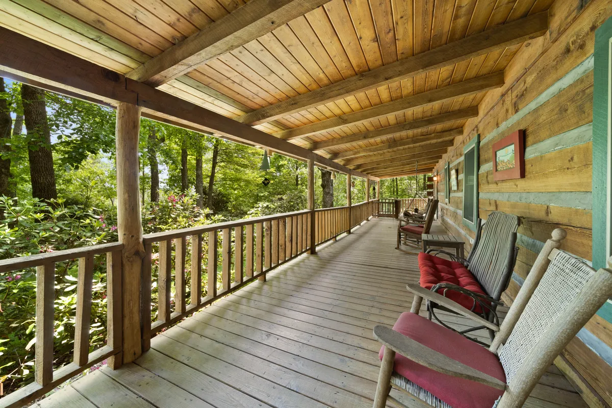 A wide, spacious porch with classic wooden rocking chairs overlooks vibrant natural greenery. The atmosphere is calm and serene, suggesting a place for morning coffee, conversation, or quiet reflection while immersed in the sights and sounds of nature.