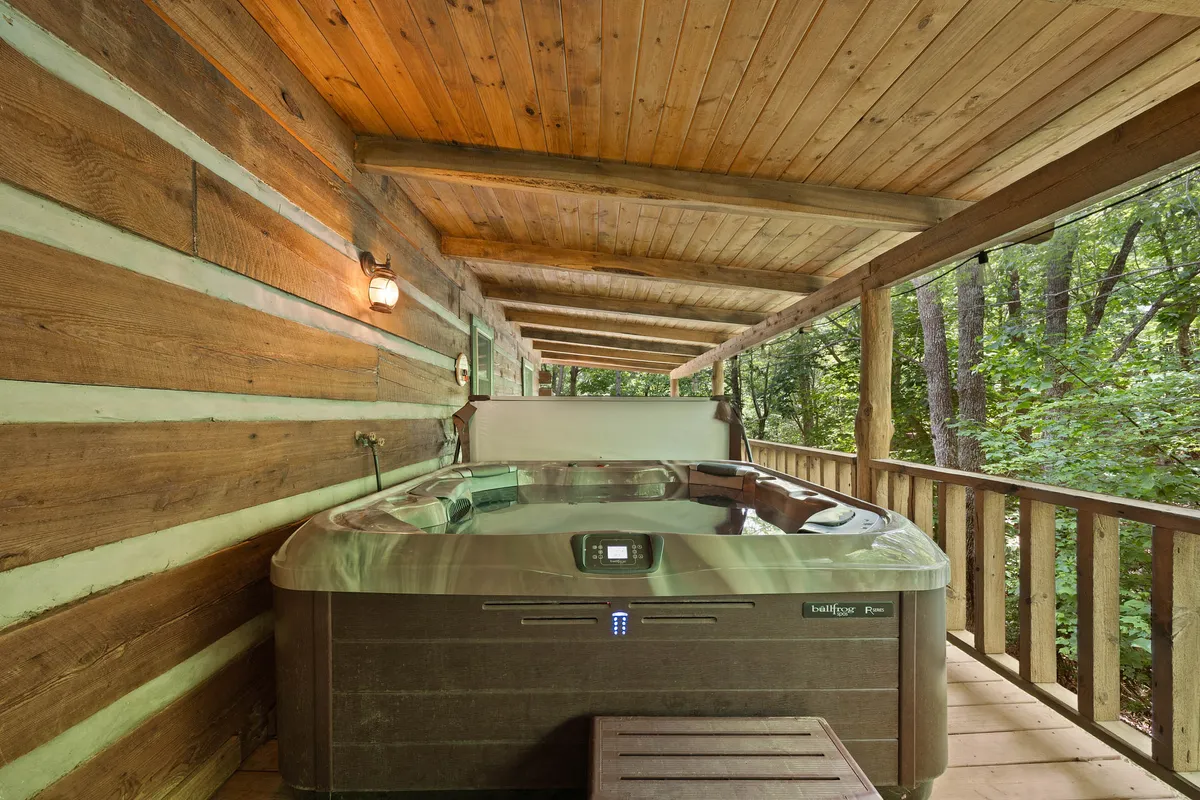 A spacious hot tub sits on a wooden deck, framed by sturdy log cabin walls and beams, offering a tranquil environment for relaxation. The view opens up to the outdoors, emphasizing a blend of comfort and immersion in nature.