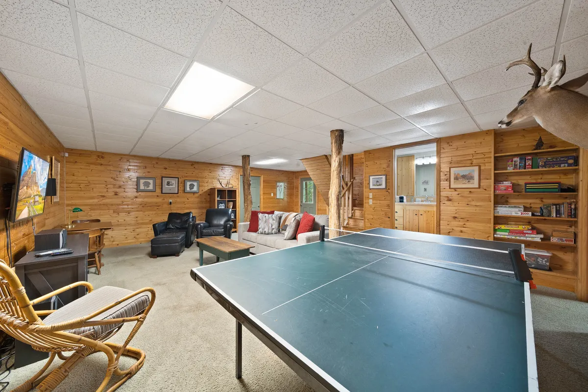 A relaxed and playful game room with a ping pong table set against wooden walls. A comfortable sofa seating area provides a spot to unwind and watch the TV mounted on the wall. The space is open and welcoming, encouraging group activities like watching sports or socializing after a game.